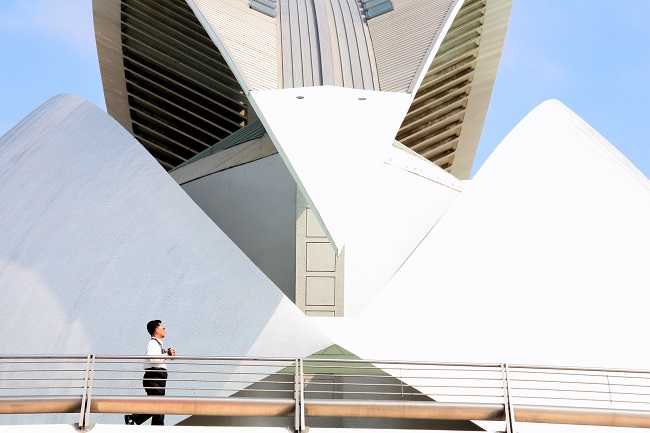 n turista creua per un pont de la Ciutat de les Arts i les Ciències de València, obra de Santiago Calatrava, amb part de l'estructura del qüestionat edifici de l'òpera, el Palau de les Arts, al fons.