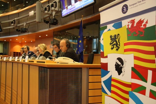 Un cartell amb les banderes de Catalunya, Gal·les, Escòcia i Euskadi durant el seminari sobre discriminació lingüística al Parlament Europeu. Al fons, els eurodiputats.