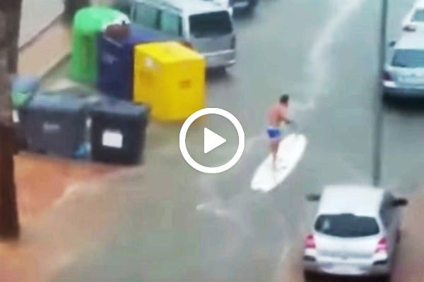 Imatge del jove surfejant pels carrers inundants per la plutja.
