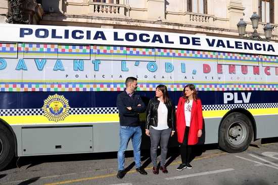 La regidora de Protecció Ciutadana Anaïs Menguzatto, al centre, acompanyada de la primera tinent d'alcalde i el regidor Carles Galiana davant l'autobus policial amb el lema 'Davant l'odi, denuncia'.