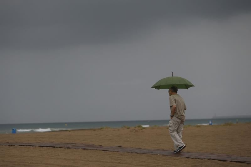 Un home passeja sota la pluja a la platja de la Malva-rosa, a València.