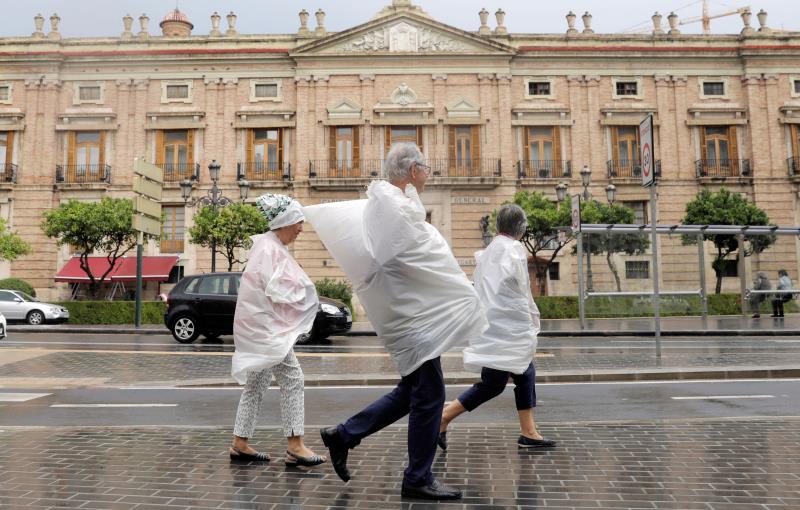 Tres persones es protegeixen amb bosses de plàstic durant una tempesta a València. Imatge d'arxiu.