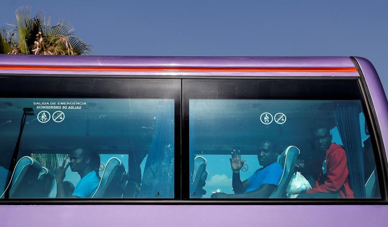 Alguns dels migrants que han partit hui cap a França saluden des de l'autobús a la seua arribada a l'aeroport de Manises.