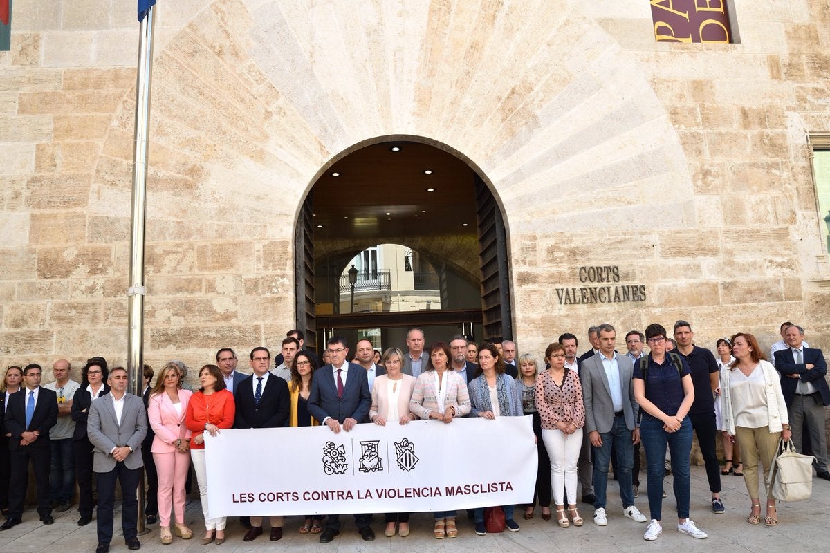 Durant el minut de silenci, en el qual els diputats dels altres cinc grups s'han situat darrere d'una pancarta conjunta, els representants de Vox s'han escorat cap a un lateral, separats de la resta de parlamentaris. / CORTS VALENCIANES