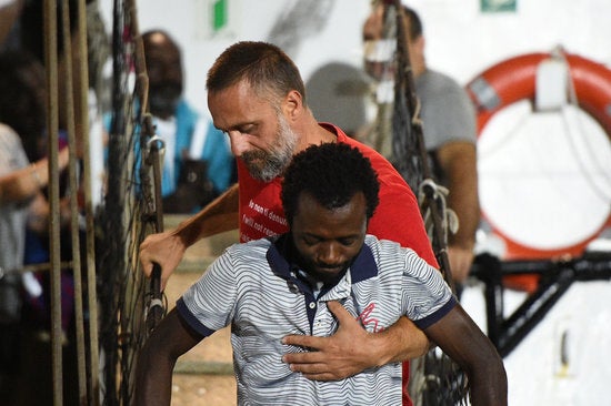 Un voluntari de l'Open Arms, ajudant a desembarcar a Lampedusa un dels migrants a bord del vaixell per ordre de la Fiscalia italiana. / REUTERS