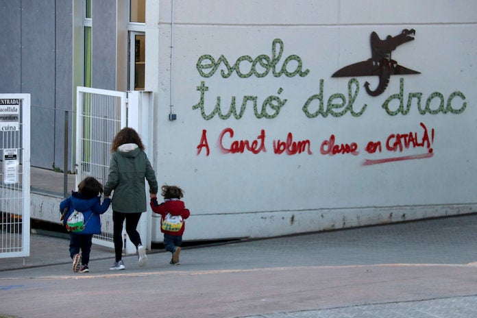 Una mare acompanya els seus fills a l'escola Turó del Drac de Canet de Mar. Una pintada reclama l'ensenyament en català a la façana del centre | Jordi Pujolar | ACN
