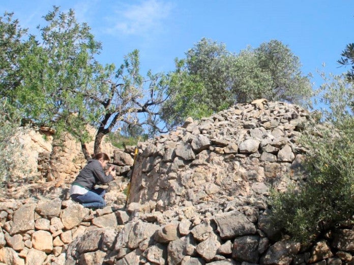 La investigadora Cèlia Mallafrè prenent mides d'una construcció de pedra en sec  | ACN