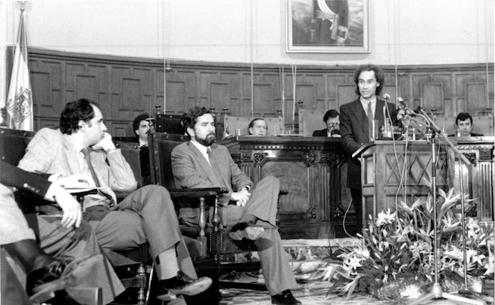 El conseller de Cultura, Ciprià Ciscar, a la tribuna, i el conseller d'Obres Públiques, Rafael Blasco, i el president de la Generalitat, Joan Lerma, asseguts, a l'esquerra, durant el ple de les Corts celebrat a Alacant el 23 de novembre del 1983



