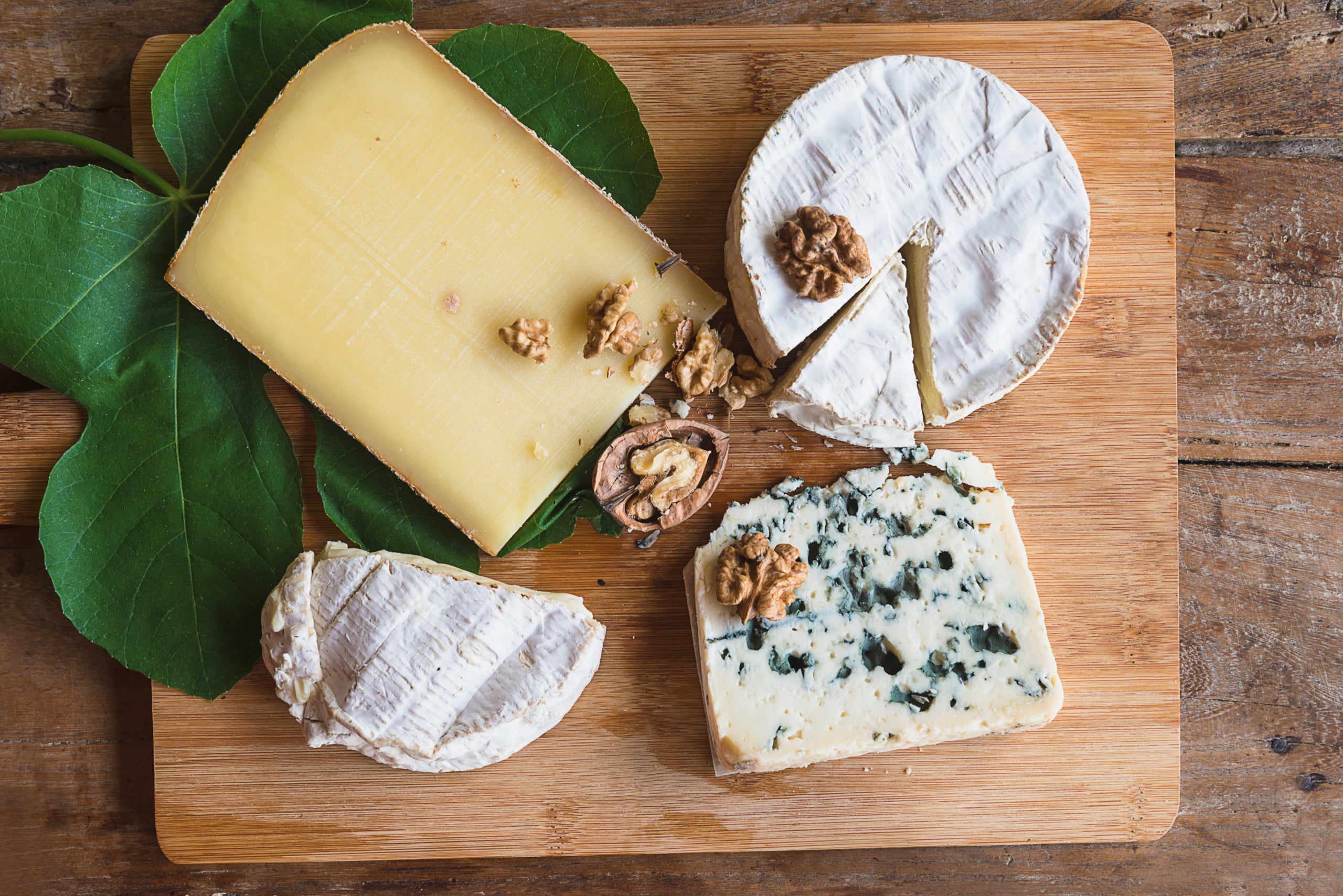 Various french cheeses, nuts, fig leaf on the wooden cutting board. Old wooden background, top view