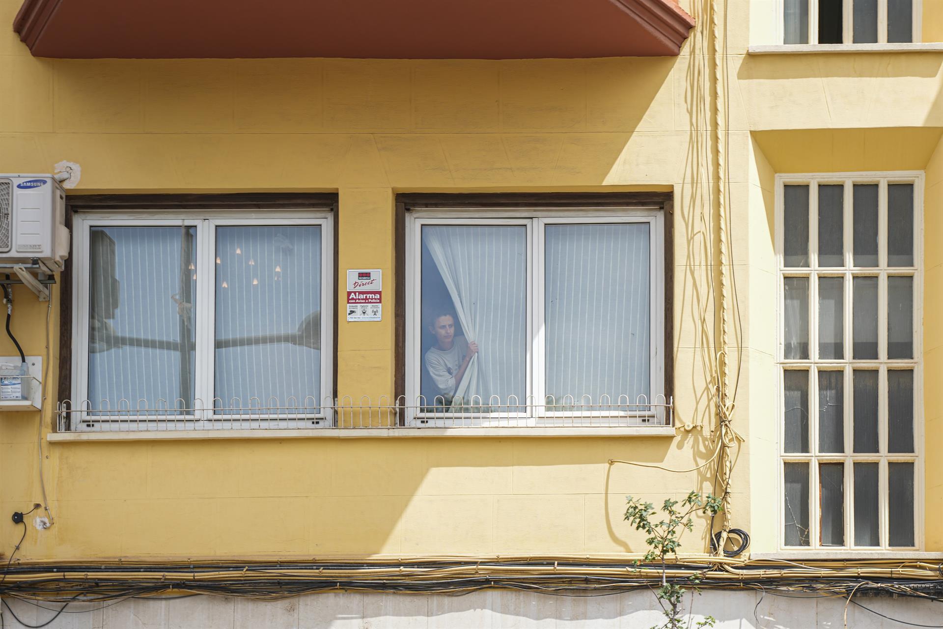 Una dona aguaita a la finestra de la casa de València de l'exministre de Transports José Luis Ábalos durant un escorcoll per part de l'UCO | Jorge Gil | EP