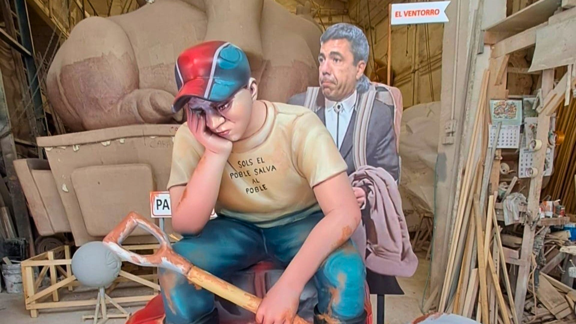 El ninot mostra a un jove cansat d'arreplegar fang mentre Mazón està al Ventorro. EP.